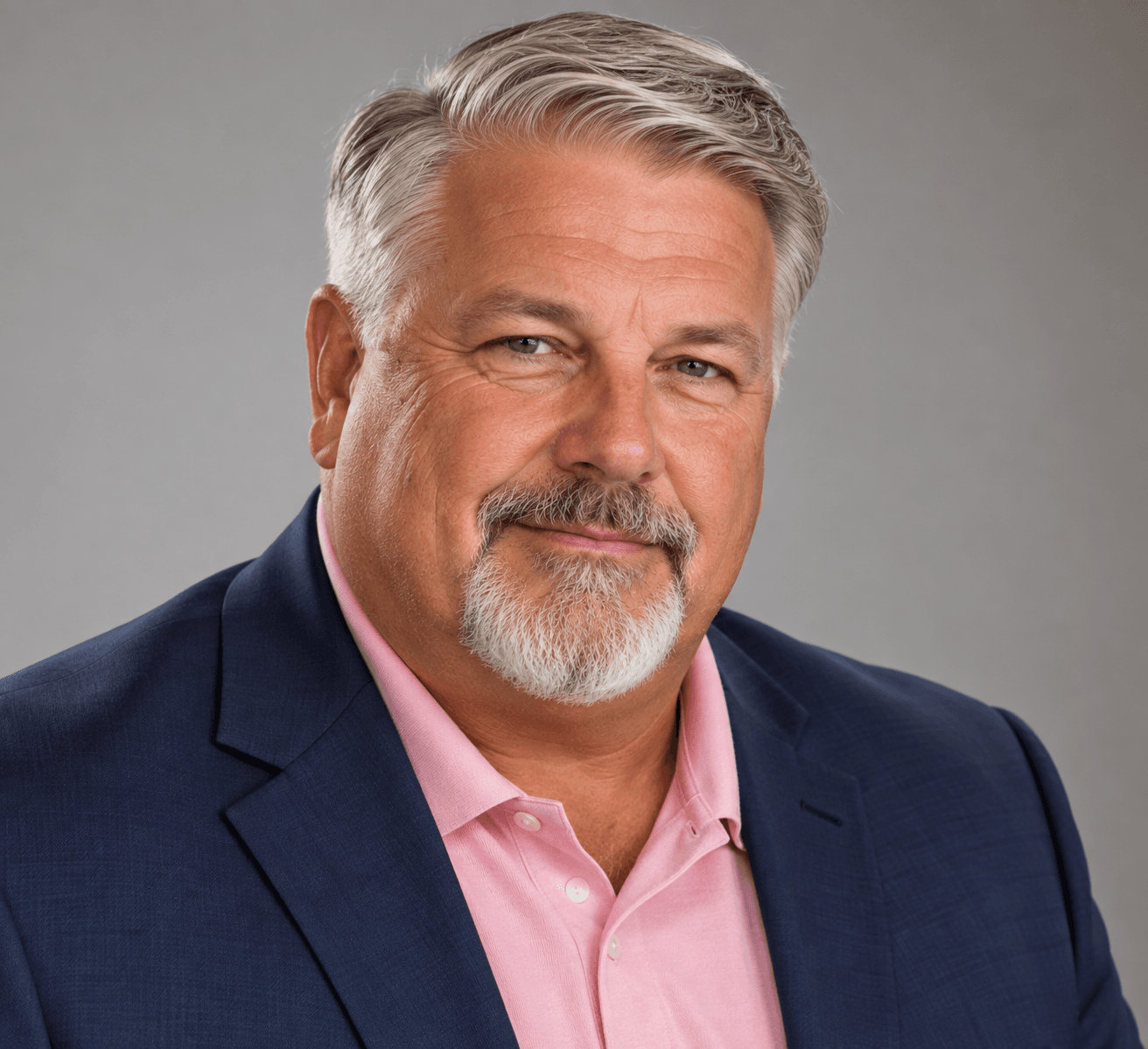 Middle-aged man with gray hair and a goatee wearing a blue blazer and pink shirt.