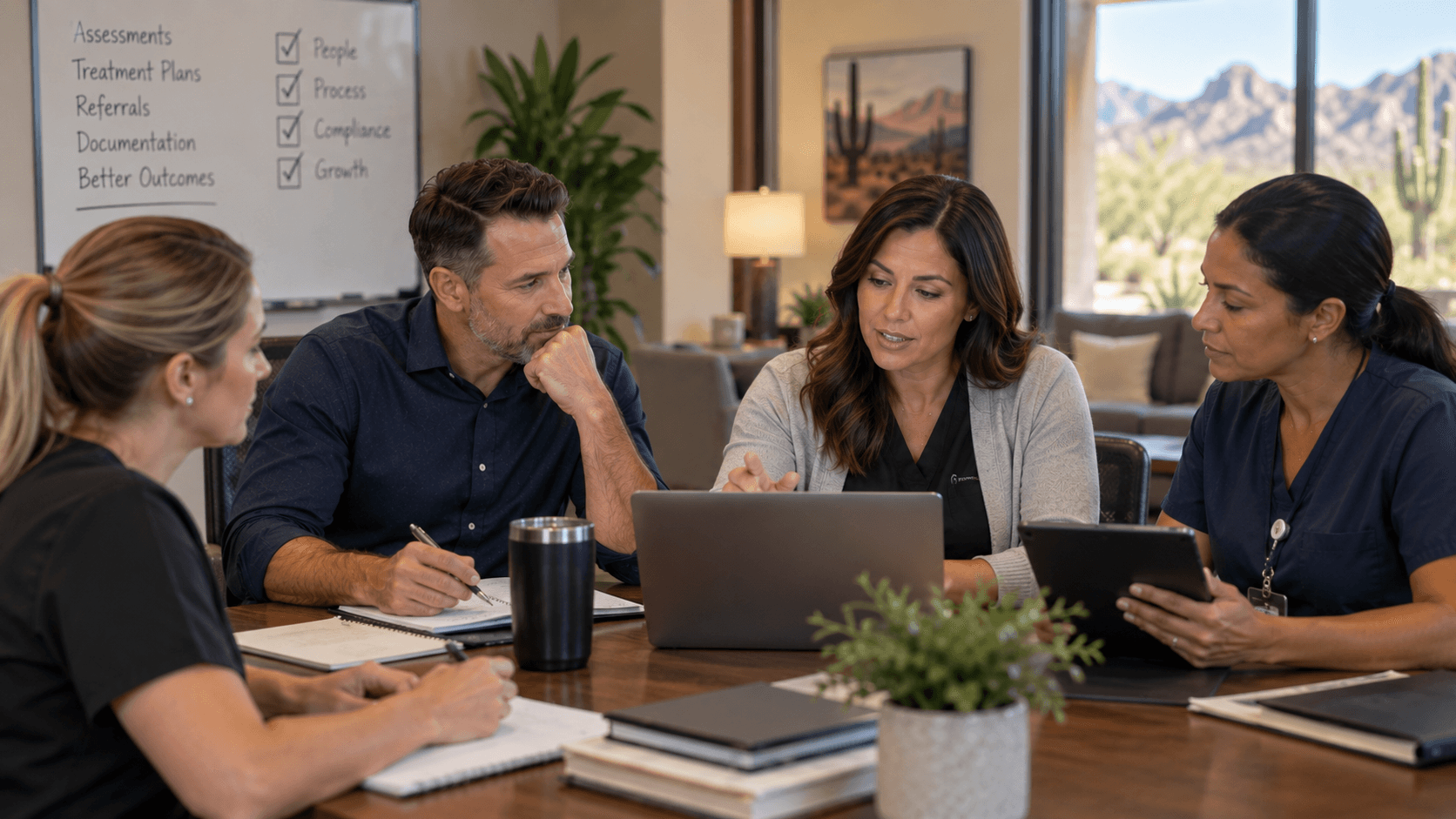 Healthcare professionals collaborate around a table with a laptop and whiteboard in a bright office.